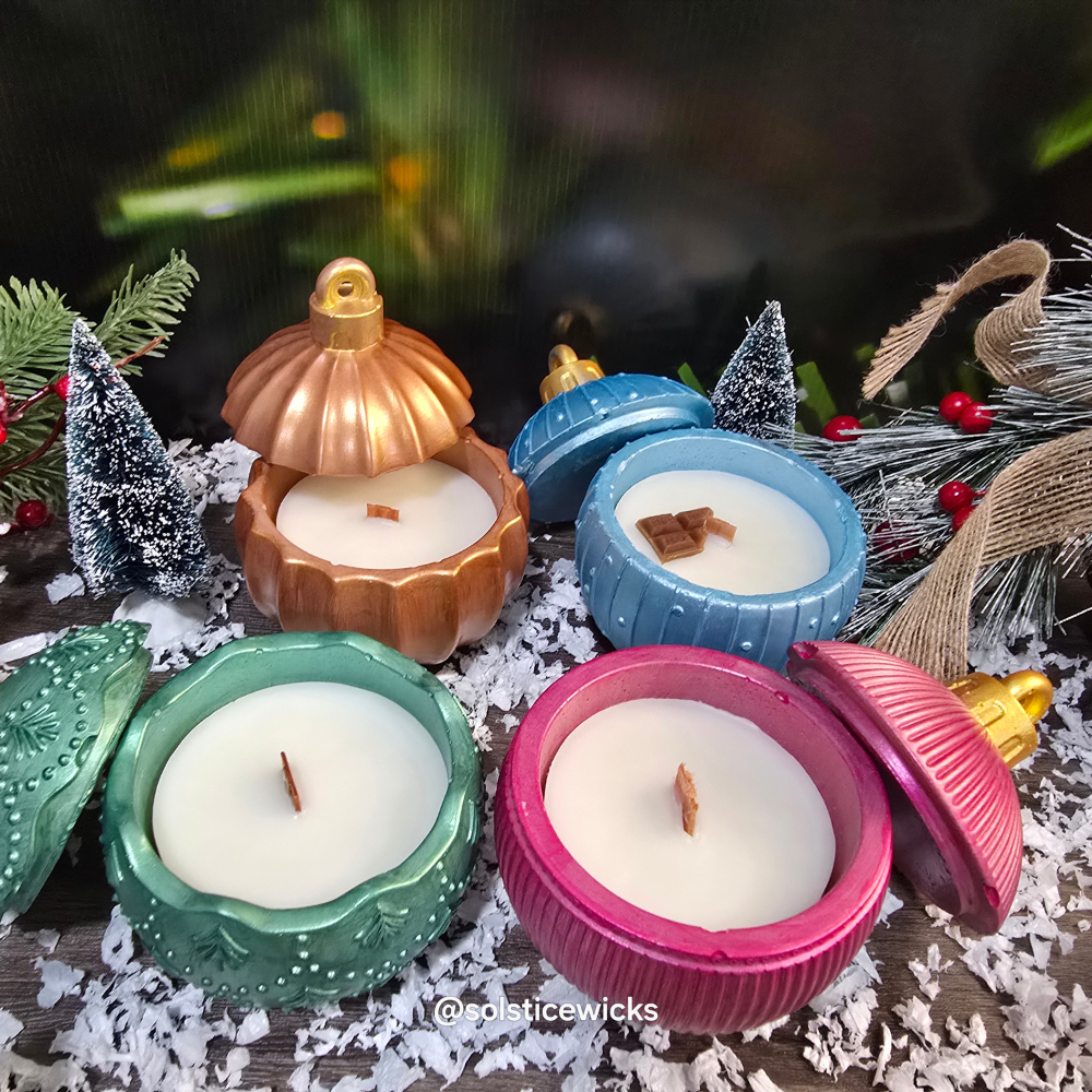 Decorative candles shaped like Christmas ornaments on a festive background with trees and lights.