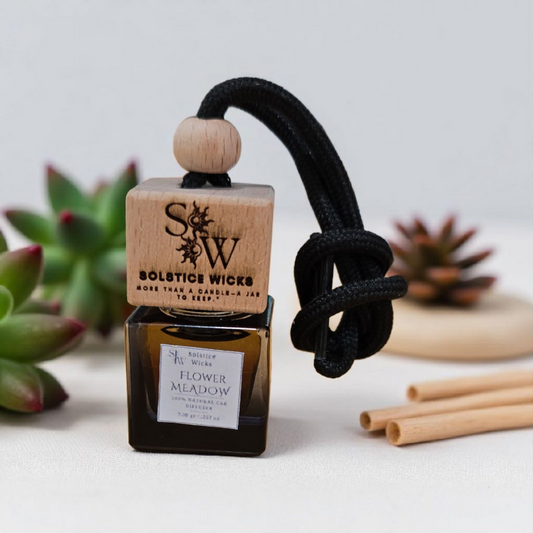 Hanging car diffuser labeled “Flower Meadow” with wooden cap and rope, surrounded by geranium, lavender, and chamomile — floral essential oil scent for car aromatherapy.