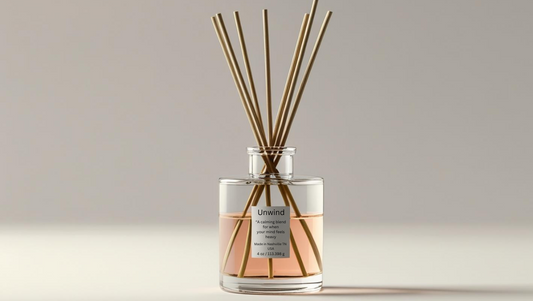 Glass reed diffuser labeled “Unwind” with mandarin slices, rose petals, lavender sprigs, and vetiver roots — a soothing natural aromatherapy blend.